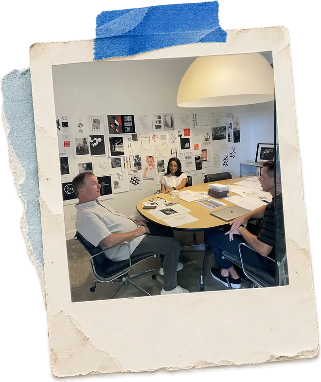 Zainab in a studio meeting, reviewing printed work around a table.